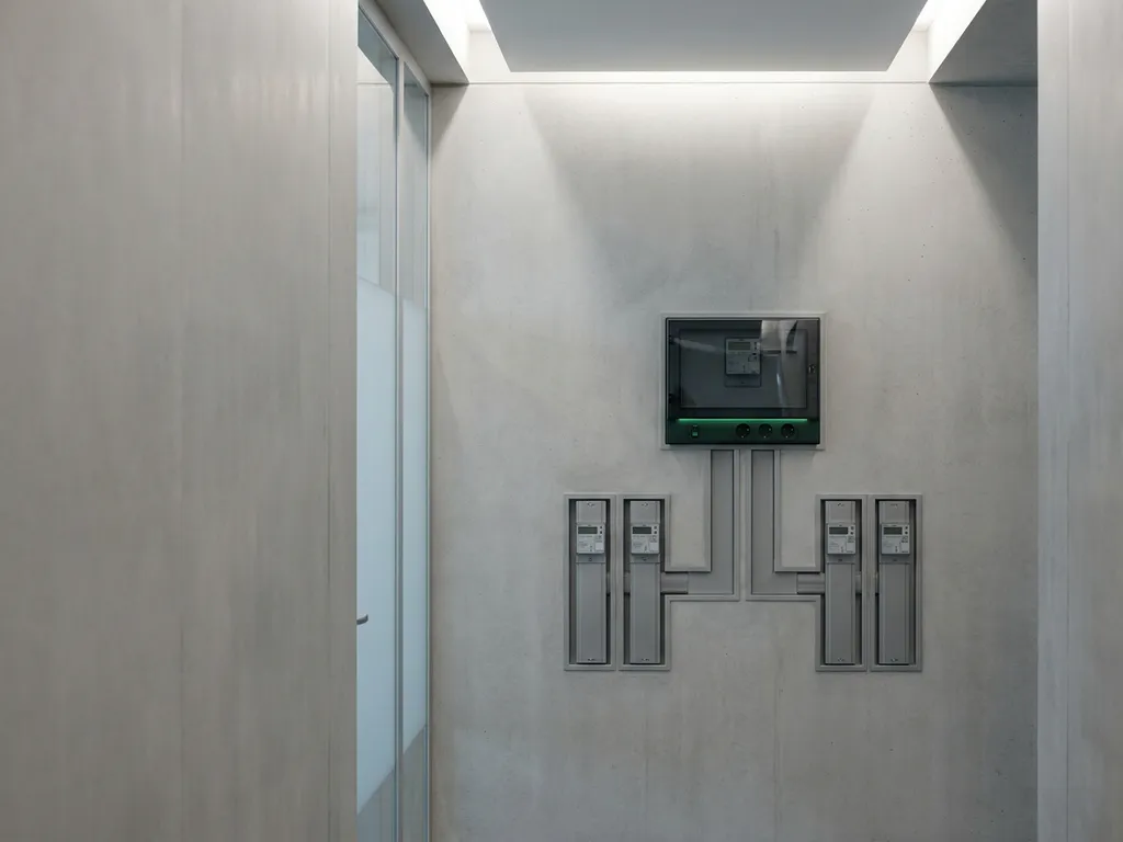 Precisie-energiemeter op betonnen wand in moderne kantoorgang met symmetrisch vertakte submeters en minimalistisch design.