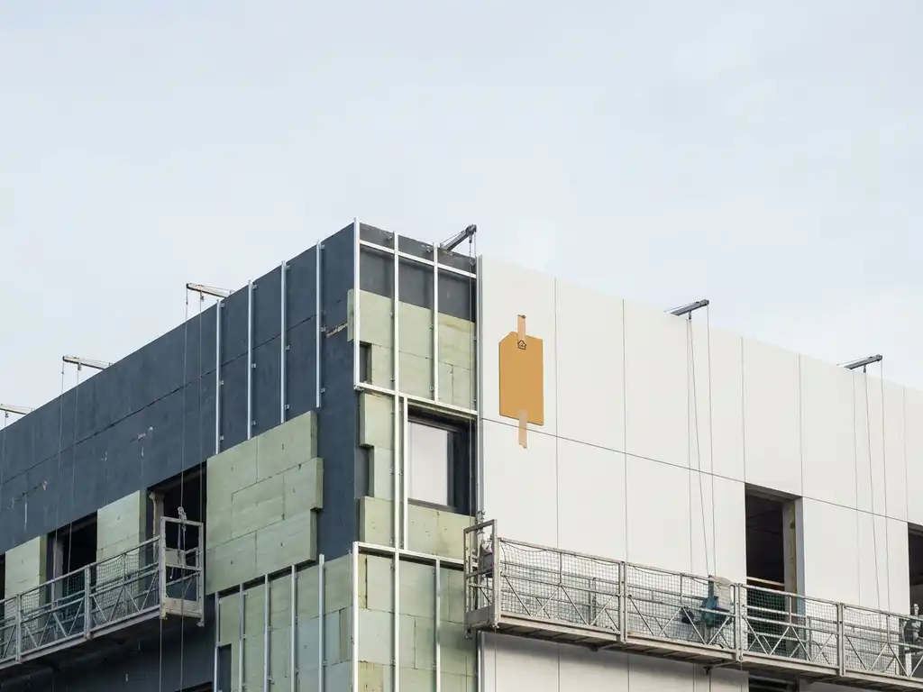Kantoorgebouw in renovatie met gedeeltelijk geplaatste isolatiepanelen en een energielabel tegen witte gevelbekledng.